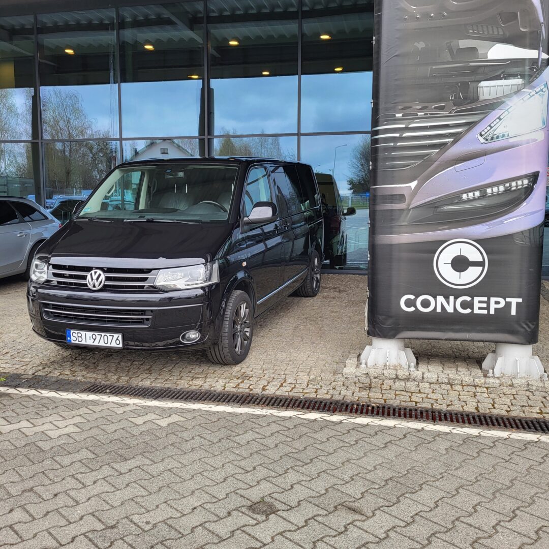 Czarny Volkswagen Multivan 2.0TDI 4Motion DSG Highline 2012 zaparkowany przed budynkiem.