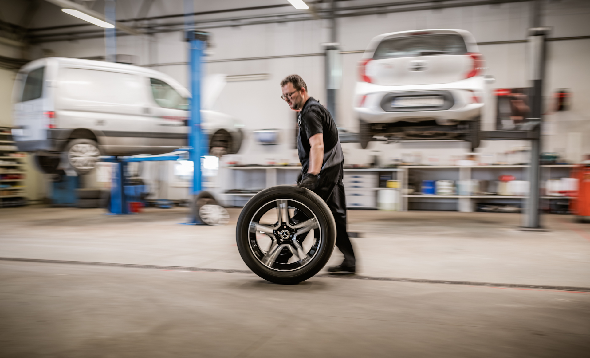 Mechanik niosący felgę aluminiową Mercedesa-Benz w warsztacie samochodowym.