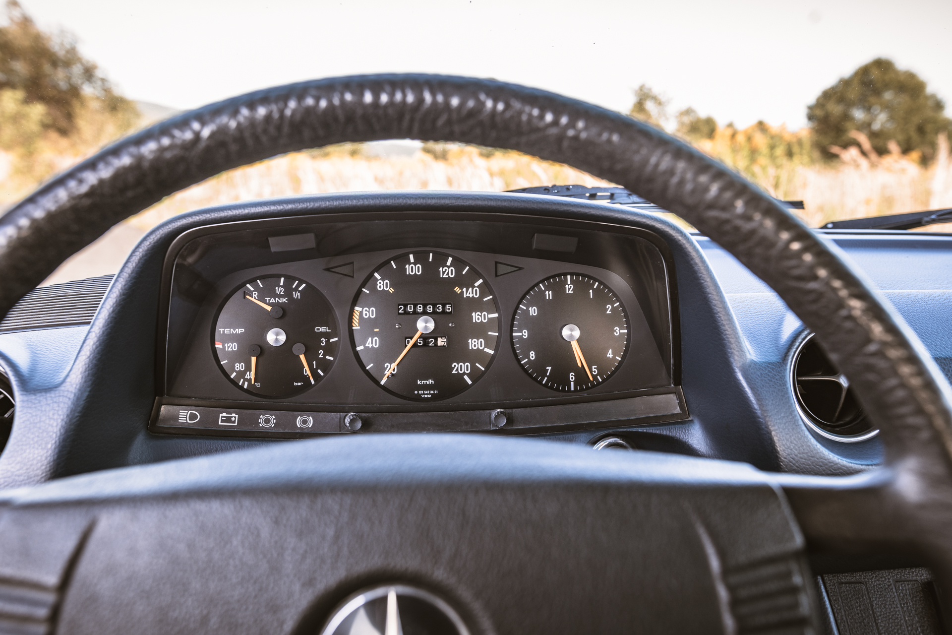 Deska rozdzielcza Mercedes-Benz W123 z widocznymi wskaźnikami prędkościomierza, obrotomierza i paliwa.