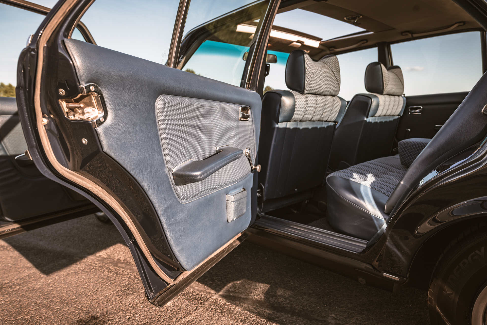 Wnętrze sedana Mercedes-Benz W123 z niebieską tapicerką i otwartymi drzwiami.