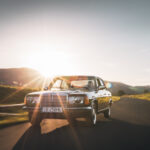 Klasyczny Mercedes-Benz W123 w kolorze czarnym jadący w słońcu.