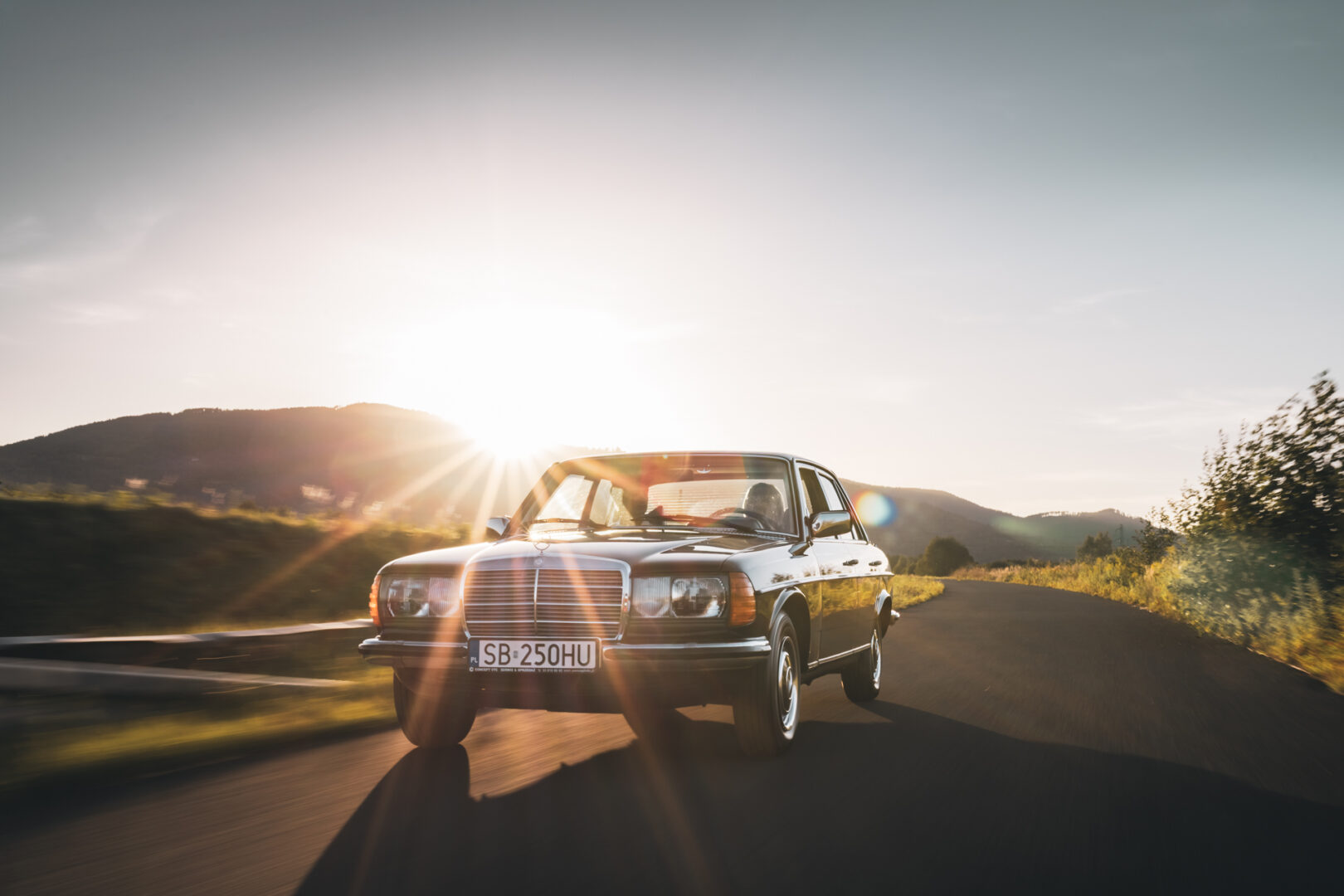Klasyczny Mercedes-Benz W123 w kolorze czarnym jadący w słońcu.