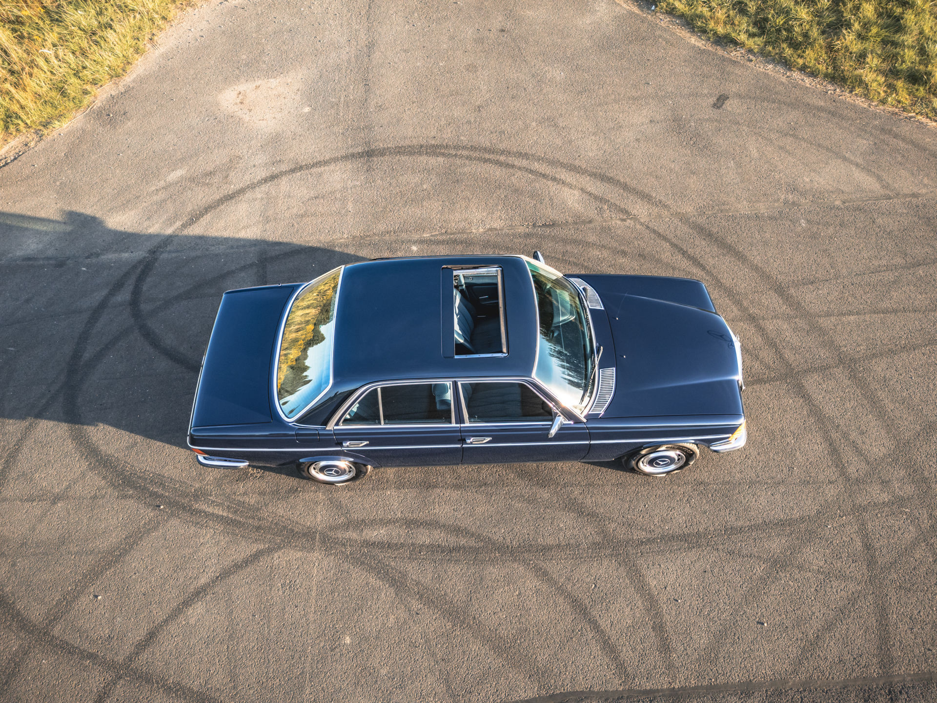 Granatowy Mercedes-Benz W123 sedan z szyberdachem, widok z góry na asfalcie.